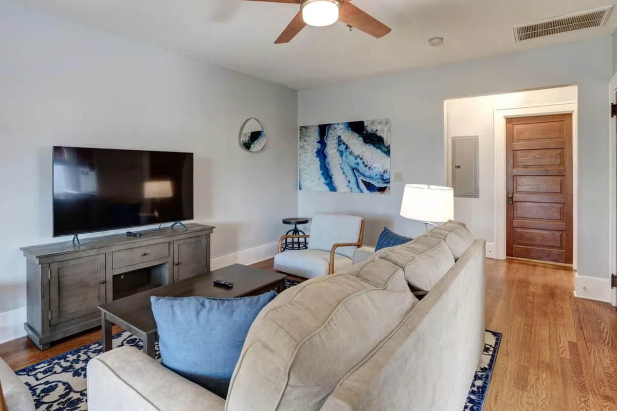 A welcoming living room featuring a comfortable sofa, a coffee table perfect for relaxing or casual work, a television for evening downtime, and tasteful artwork on the wall. Soft lighting from a nearby lamp gives the space a cozy, inviting atmosphere.