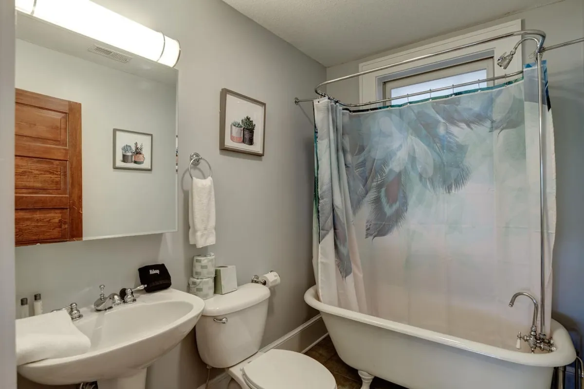 A modern, inviting bathroom featuring a classic clawfoot bathtub with a floral shower curtain, a wooden cabinet, and a decorative mirror. The space suggests both functionality and the opportunity for indulgent self-care.