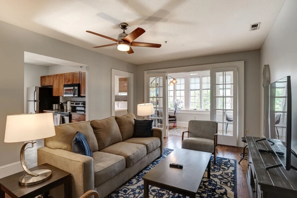 The image shows another perspective of the living room, focusing on a comfortable sofa, a sleek coffee table, a TV, and a stylish light fixture. This layout creates a welcoming atmosphere ideal for relaxation or socializing with friends.