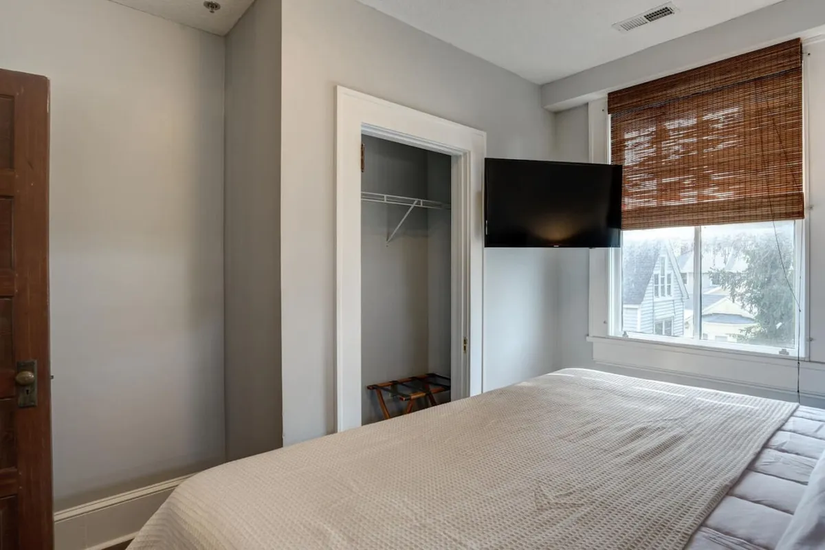 Another inviting bedroom with a king bed, a window letting in natural sunlight, a wall-mounted television, and a tidy closet. The environment feels tranquil and organized, ideal for both relaxation and privacy.