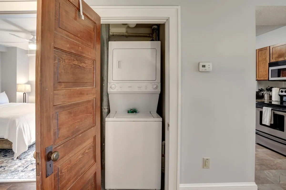 A practical view of the apartment’s washer and dryer set next to a wooden door, with kitchen appliances visible in the background. This scene hints at everyday convenience that makes longer stays comfortable and stress-free.
